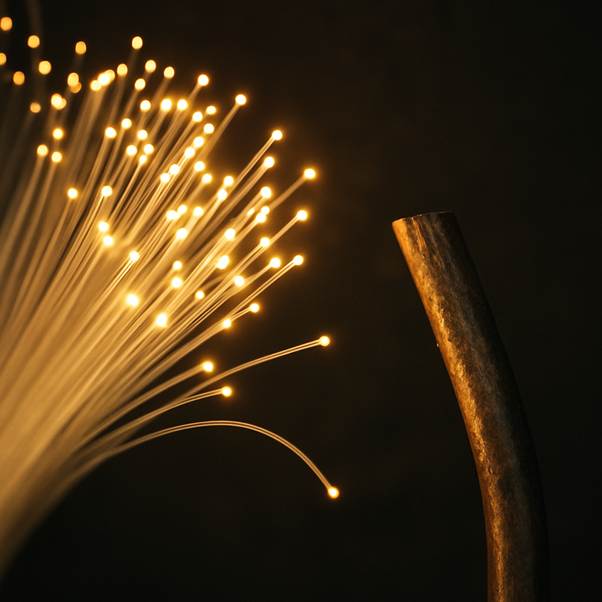 A close-up shot of a glowing fibre optic cable bundle with light emanating from the tips, contrasted against an old, dull copper wire.